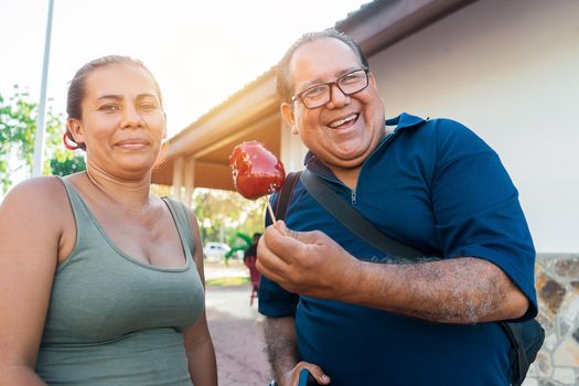 Mature man flirting with a green-eyed woman with a caramel apple in a park in the city of Managua.