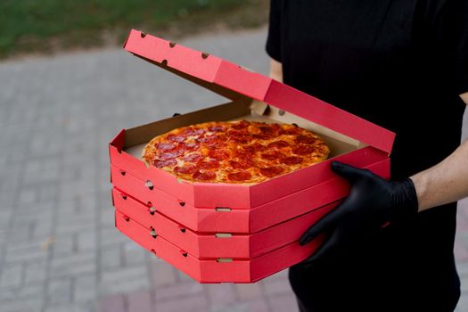 Safety pizza delivery from restaurant. Food courier in black medical gloves. Isolated photo of pizza with cheese and salami. Stop pandemic coronavirus covid 19.