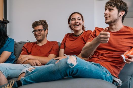 friends sitting on the sofa watching TV and laughing. watching a film. watching sport on TV. sitting on the sofa in the living room, natural light.