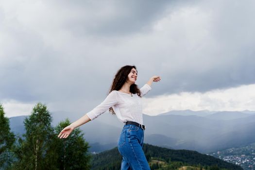 Feeling freedom in Karpathian mountains. Tourism travelling in Ukraine. Girl girl raised her hands up and enjoys the mountain hills view.