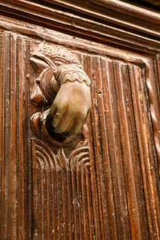 Golden doorknocker with hand shape on old brown wooden door in Villajoyosa, Alicante, Spain