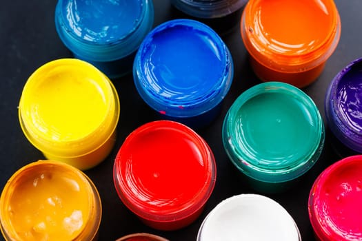 full-frame close-up background of opened small gouache paint jars on black backdrop