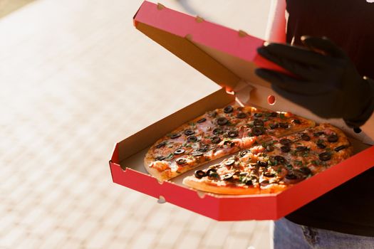 Safety pizza delivery from restaurant. Food courier in black medical gloves. Isolated photo of pizza with cheese and salami. Stop pandemic coronavirus covid 19