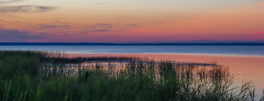 Beautiful pink sunset on the lake. Water sky coast horizon reeds.