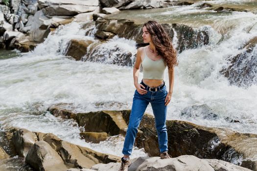Girl is travelling in Karpathian mountains and feeling freedom. Waterfall in mountain river. Cascade waterfall and beautiful young woman