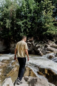 Traveler man on the rock near waterfall. Travelling in Karpathian mountains. Cascade waterfall. Beautiful landscape