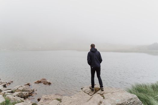 Man tourist is travelling and standing on the rocks near foggy lake. Hiking and climbing up to the top of the mountain. Tourism in Ukraine.