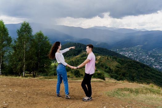 Girl points her boyfriend at rain far away. Couple looking at the mountain hills before raining. Feeling freedom together in Karpathian mountains.