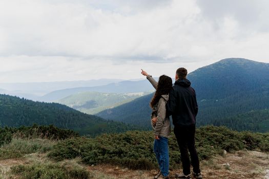 Couple at the peak of the mountain. Girl is pointing to the sky. Lifestyle of travelling people. Love story in the mountains