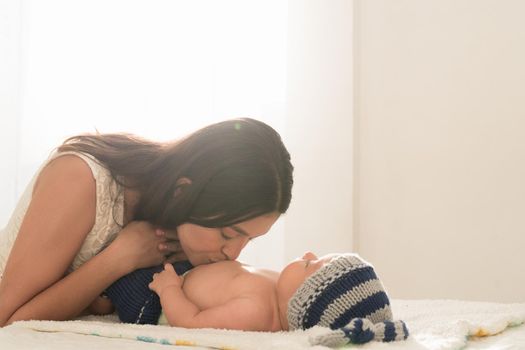 Latin young mother kisses her baby in the small belly on the bed at home. High quality photo horizontal photo style life