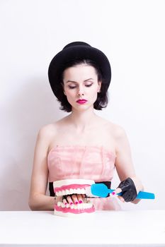 A woman in a dress and hat sits at a table and holds a mock-up of her teeth. High quality photo