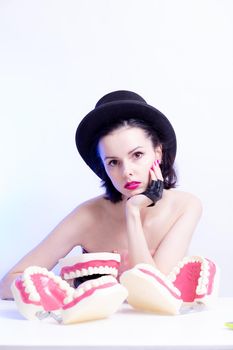 A woman in a dress and hat sits at a table and holds a mock-up of her teeth. High quality photo