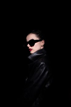 woman in leather coat and black sunglasses, black background. High quality photo