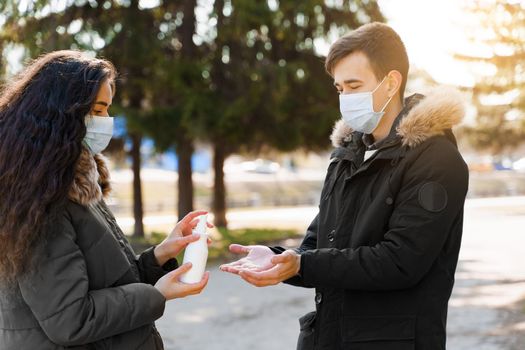 Man and women in medical mask spay each other antiseptic for disinfection hands. Life after pandemic of coronavirus covid 19