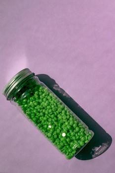 green wax for depilation in granules. on a purple background. jar with wax on isolated background.