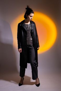 a woman in a black leather coat, in high-heeled shoes illuminated by colored light. High quality photo