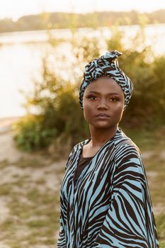 Confident muslim black girl weared in hijab smiles. African woman in national colorful dress on green background