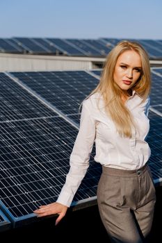 Woman leans on solar panels. Blonde dressed white formal shirt on the power plant. Free electricity for home. Green energy.