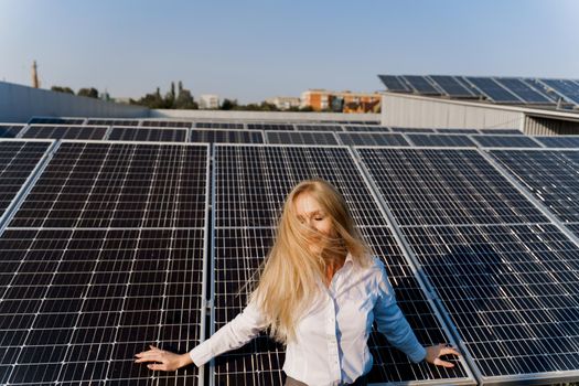 Woman leans on solar panels. Blonde dressed white formal shirt on the power plant. Free electricity for home. Green energy.
