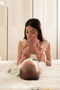 Latin young mother kisses whith love baby feet and sniff them on the bed at home. High quality photo vetfical photo style life