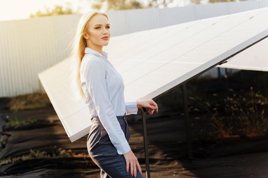Girl stand near solar panels row on the ground with sun light. Woman investor wears formal white shirt. Free electricity for home