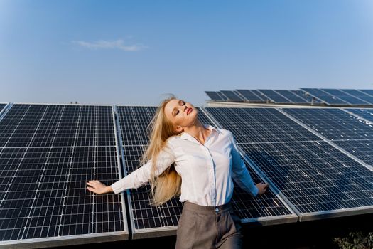 Woman leans on solar panels. Blonde dressed white formal shirt on the power plant. Free electricity for home. Green energy.