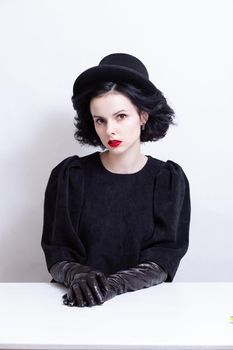 a woman with red lips, curly hair in a black hat and gloves sits at a table. High quality photo