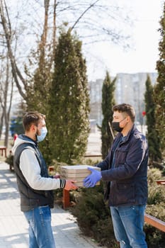 Courier in medical gloves gives 4 pizza boxes to customer who sick coronavirus covid 19. Safety food delivery form pizza restaurant