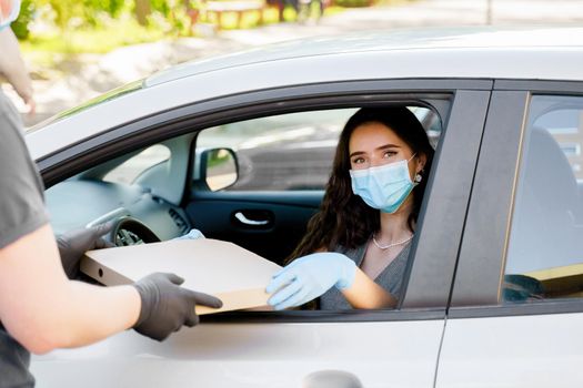 Food delivery courier gives pizza to woman in eco car. Tasty pizza with salami, cheese, tomatoes in cardoard box. Giving food trought car window