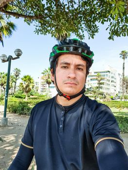 young handsome cyclist in black cycling clothing, wearing a helmet in a park