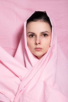 portrait of brunette woman wrapped in pink cloth, pink background. High quality photo