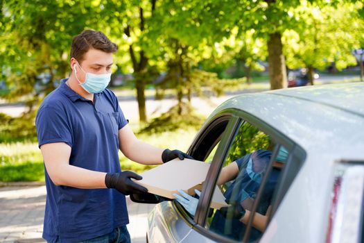 Safety pizza delivery from pizzeria trought car window during quarantine covid 19. Business woman in medical mask and gloves gets food in carton box