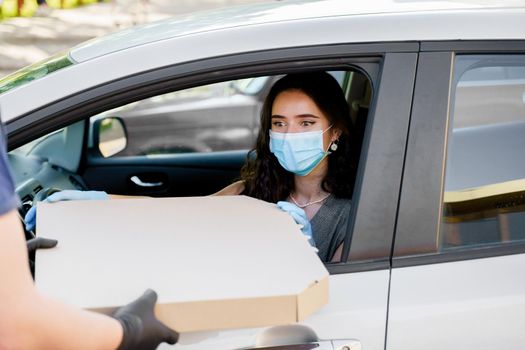 Food delivery courier gives pizza to woman in eco car. Tasty pizza with salami, cheese, tomatoes in cardoard box. Giving food trought car window