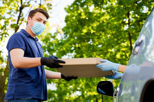 Food delivery courier gives pizza to woman in eco car. Tasty pizza with salami, cheese, tomatoes in cardoard box. Giving food trought car window