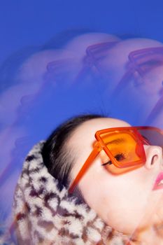 Art portrait, a woman with pink lips in orange glasses and a leopard hoodie on a blue background. High quality photo
