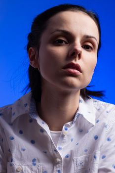 brunette woman in a white shirt with polka dots, on a blue background. High quality photo