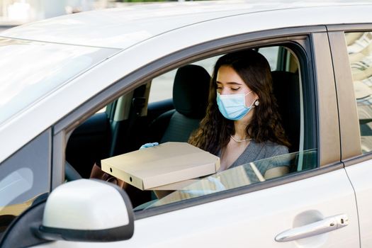 Lovely caucasian girl with green eyes looks at pizza and wants to eat. Courier in medical mask and gloves.