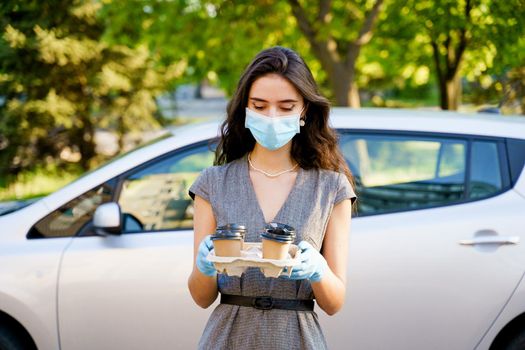 Coffee from coffee shop delivery by car. Coffee in eco disposable cardboard cup. Young girl works in delivery agency. 4 coffee in hands.