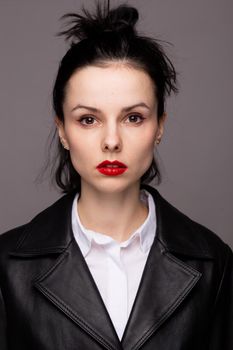 brunette woman with red lipstick on her lips in a black leather jacket and white shirt, grey background. High quality photo