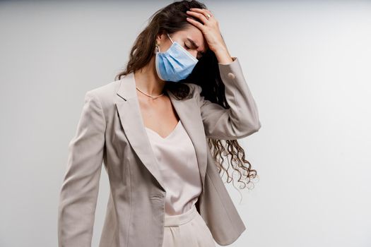 Headache girl in blue medical mask. Woman touches her head because sicks coronavirus covid-19. Attractive girl weared white formal dress