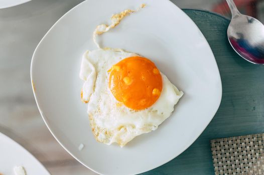 Top view of white plate with fried egg on glass table background