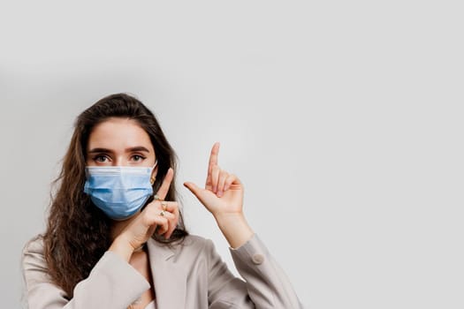 Coronavirus covid-19 quarantine concept. Attractive girl in blue medical mask points up isolated on white background.