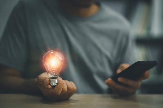 Businessman holding a bright light bulb and using mobile phone. Concept of Ideas for presenting new ideas Great inspiration and innovation new beginning.