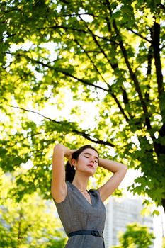 Relaxation and meditation lifestyle of young girl in green park. Vertical photo of beautiful girl who touches and correct her hair.