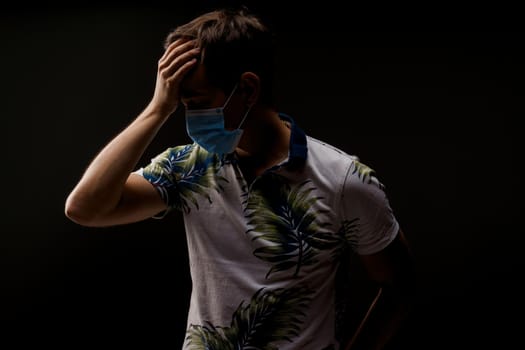 Headache man in blue medical mask isolated black background. Man touches her head because sicks coronavirus covid-19. Pandemic 2020.