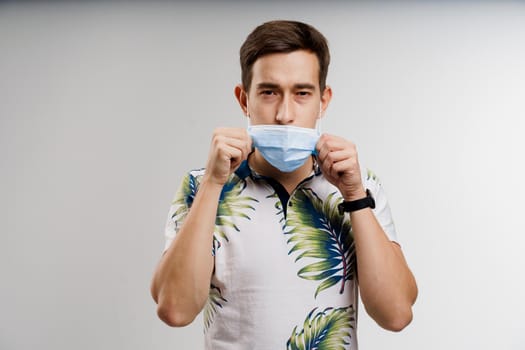 Handsome man touches medical mask in quarantine covid-19 period. Man weared t-shirt isolated white background. Coronavirus concept