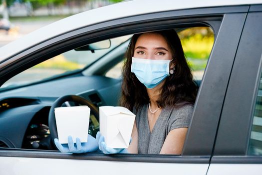 Udon noodles in white box delivery. Young attractive girl in car in medical gloves and mask holds wok in box udon noodles and smiles