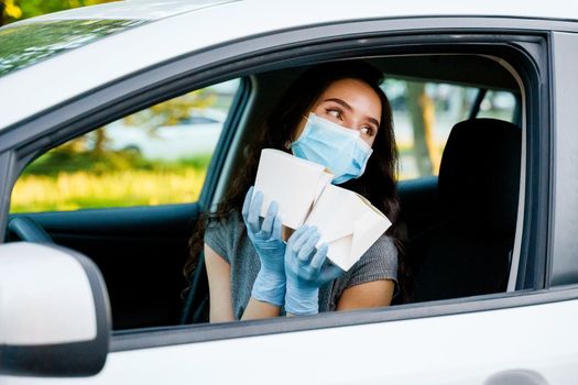 Udon noodles in white box delivery. Young attractive girl in car in medical gloves and mask holds wok in box udon noodles and smiles