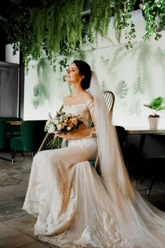 Bride in wedding dress and bridal veil seats on fashion chair in cafe. Advert for social networks for wedding agency and bridal salon.