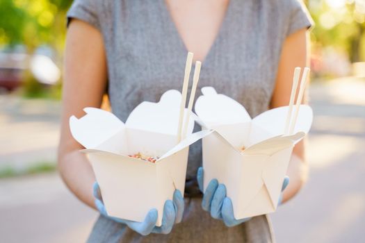 Closeup tasty food wok in box delivery. Girl holds udon noodles with tempuru, shrimps, soy sauce in hands in medical gloves